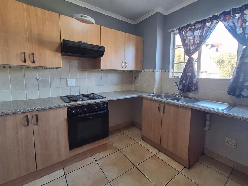 Functional kitchen featuring laminate cabinetry, built-in oven with hob, extractor fan, and double stainless steel sink with tiled backsplash and flooring.