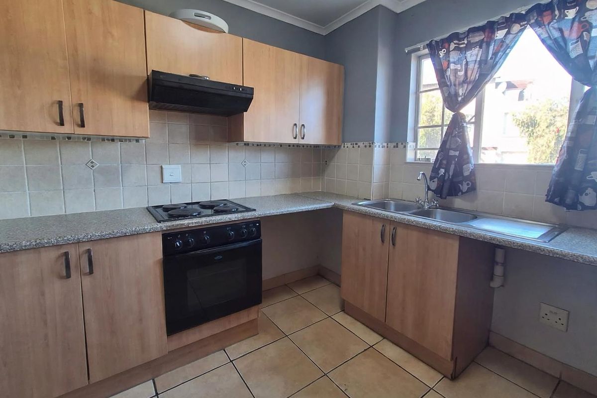 Functional kitchen featuring laminate cabinetry, built-in oven with hob, extractor fan, and double stainless steel sink with tiled backsplash and flooring.