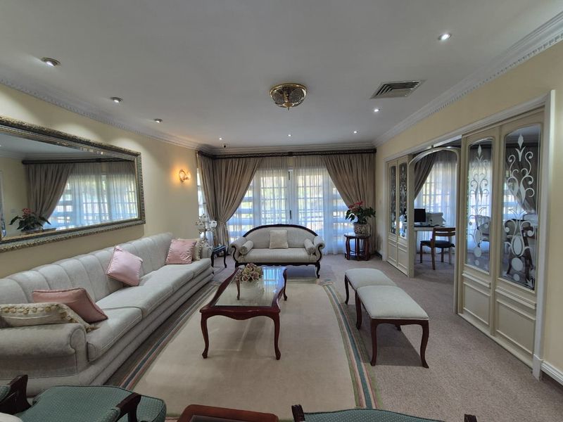 Spacious living room featuring decorative coving, recessed lighting, and elegant glass-panelled room dividers leading to an adjacent study area.