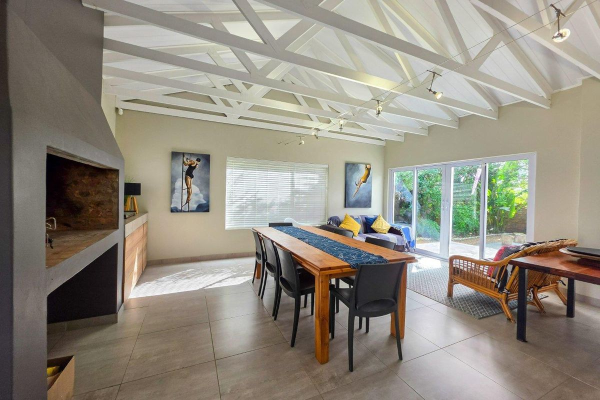 Spacious living area featuring exposed white timber rafters, large format floor tiles, a built-in fireplace, and sliding glass doors opening to the garden.