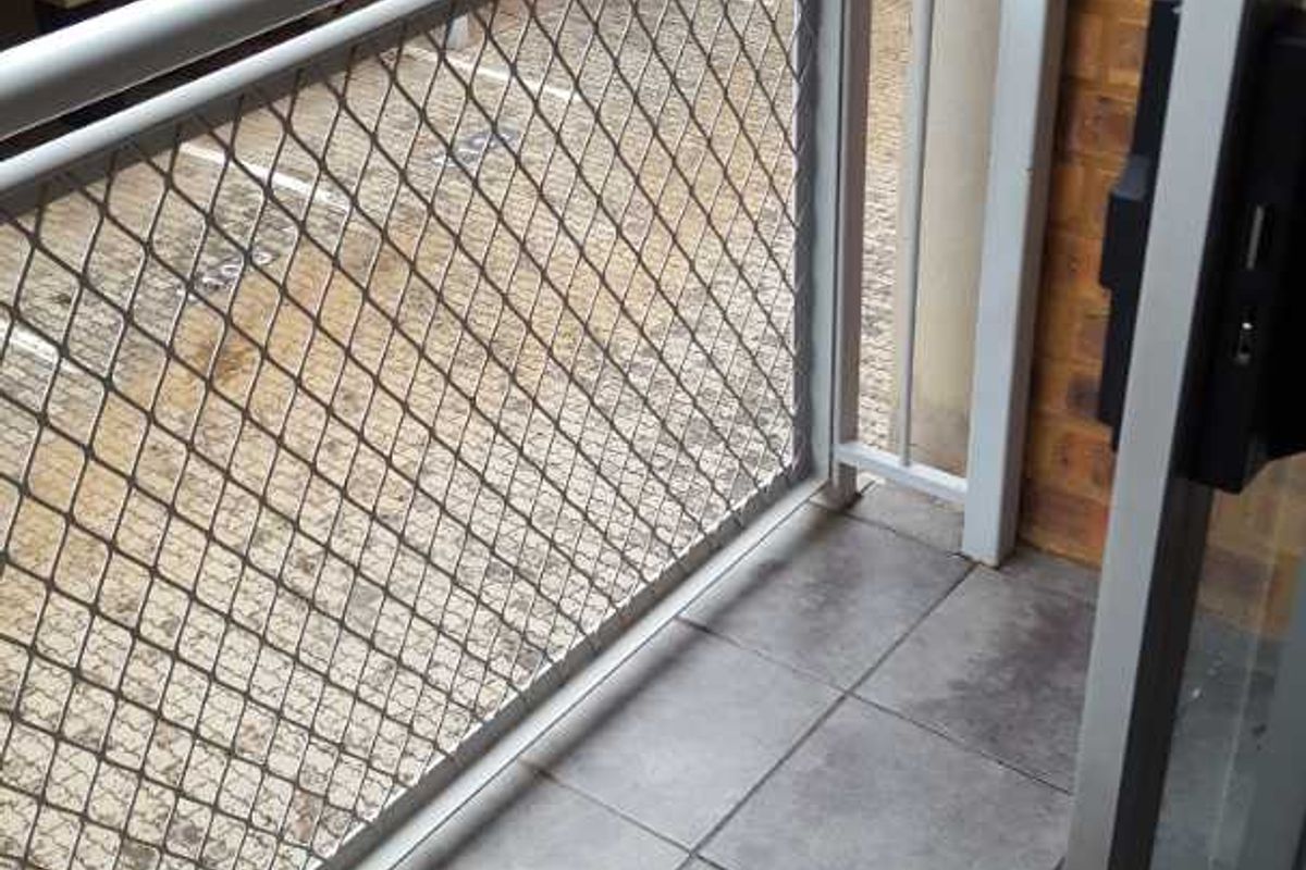 A compact balcony featuring tiled flooring and a secure metal balustrade, offering an outdoor space accessible via a sliding glass door.