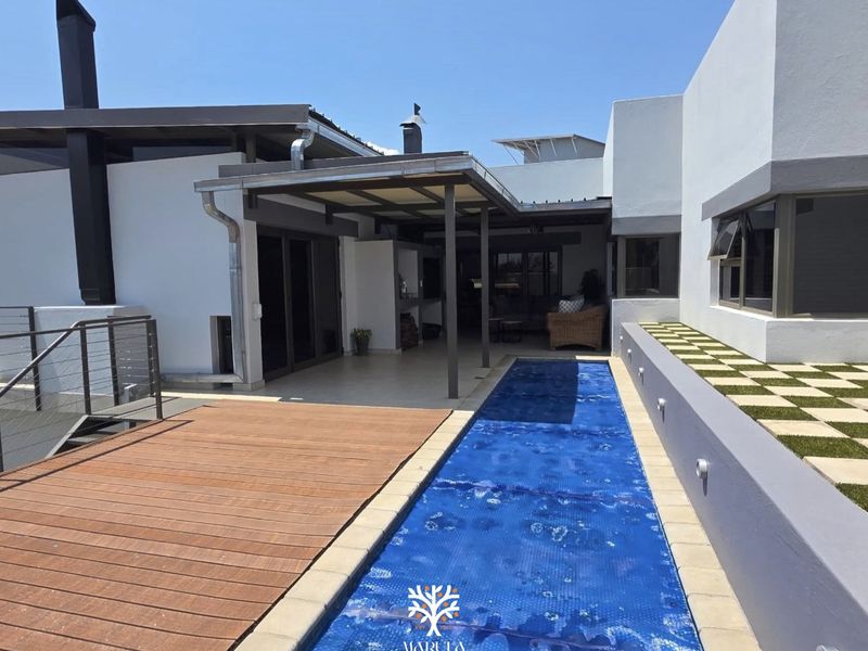 Modern outdoor entertainment area featuring a swimming pool with cover, timber decking, and a covered patio with a built-in fireplace.