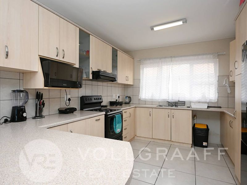 Functional kitchen featuring light wood-tone cabinetry, stone-look countertops, ceramic tile flooring, and integrated appliances including an oven and extractor fan.