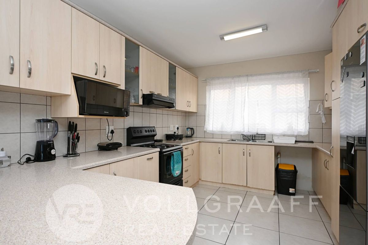 Functional kitchen featuring light wood-tone cabinetry, stone-look countertops, ceramic tile flooring, and integrated appliances including an oven and extractor fan.
