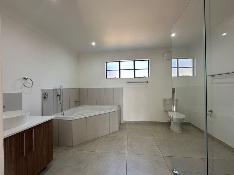 Spacious modern bathroom featuring a corner bathtub, glass-enclosed shower, vanity with vessel sink, and neutral floor tiling.