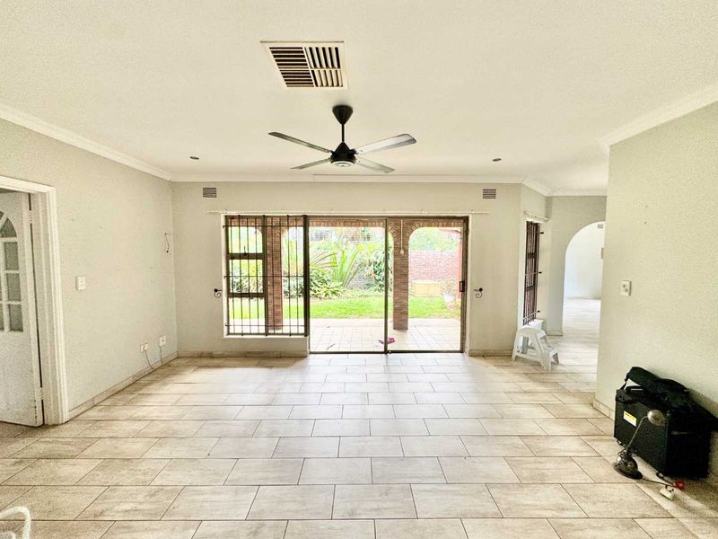 Spacious living area featuring neutral tiled flooring, ceiling fan, and large sliding glass doors providing direct access to the rear patio and garden.