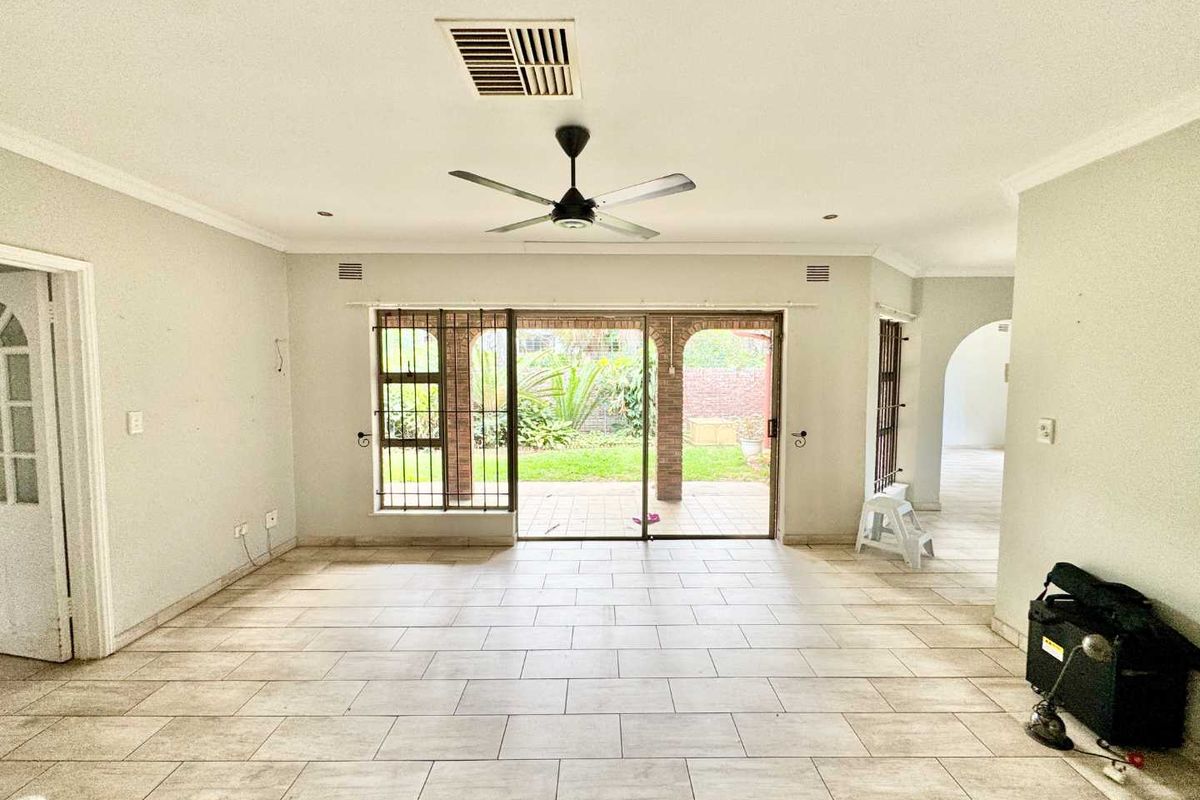 Spacious living area featuring neutral tiled flooring, ceiling fan, and large sliding glass doors providing direct access to the rear patio and garden.
