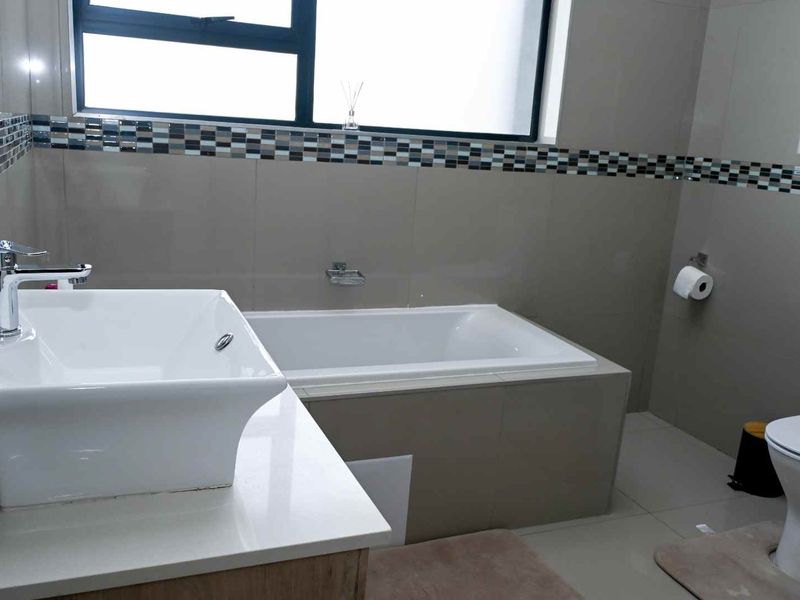 A modern bathroom featuring a built-in bathtub, a contemporary vessel sink vanity, and a wall-mounted toilet with neutral tiled finishes.