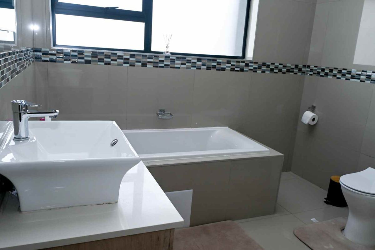 A modern bathroom featuring a built-in bathtub, a contemporary vessel sink vanity, and a wall-mounted toilet with neutral tiled finishes.