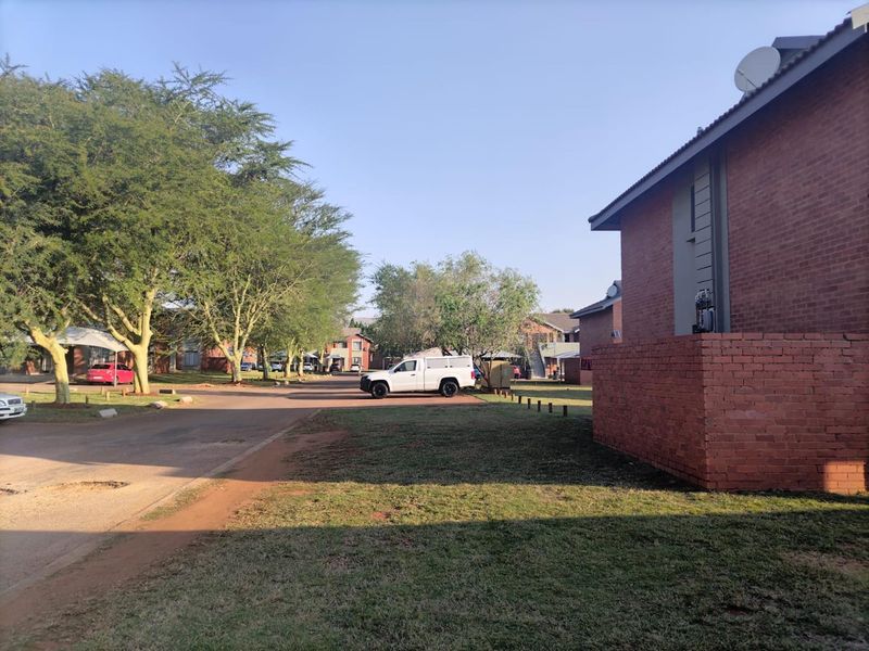 Exterior view of a brick apartment building complex with a paved driveway and surrounding landscaped grounds.