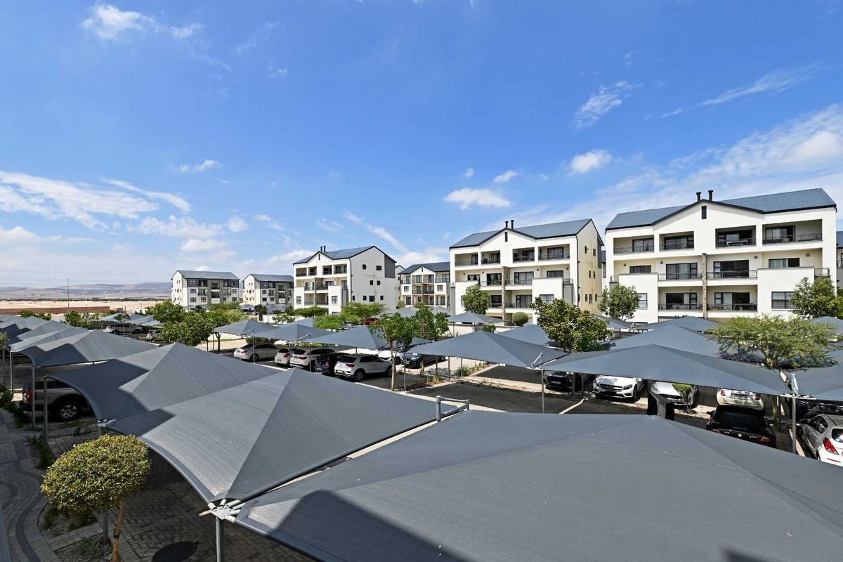 An elevated view of the apartment complex grounds, featuring paved parking areas with shade-cloth carports and landscaped surroundings.