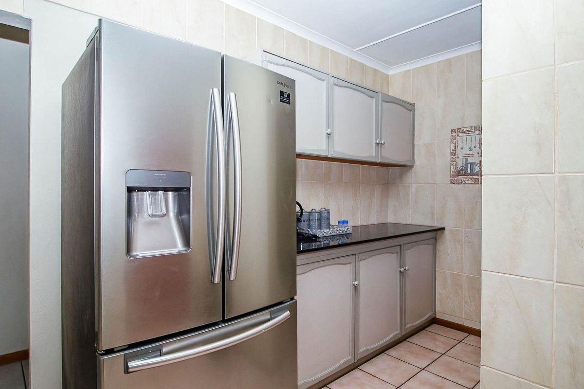A compact kitchen area featuring tiled walls, built-in cabinetry with dark countertops, and space for a large refrigerator.
