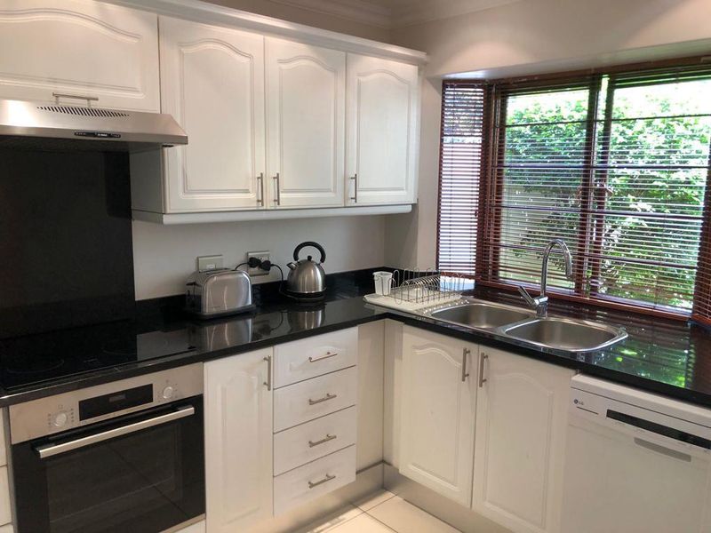 A well-maintained kitchen featuring white cabinetry, black granite countertops, a built-in oven, electric hob, and a double sink with garden views.