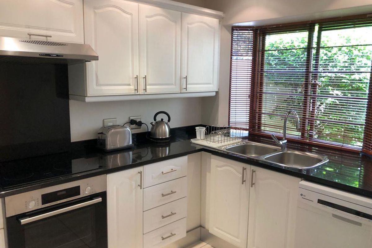A well-maintained kitchen featuring white cabinetry, black granite countertops, a built-in oven, electric hob, and a double sink with garden views.