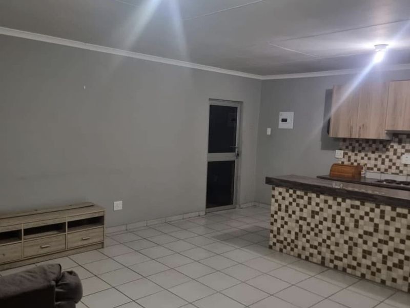 Open plan living and kitchen area featuring tiled flooring, a breakfast counter with mosaic detailing, and neutral wall finishes.