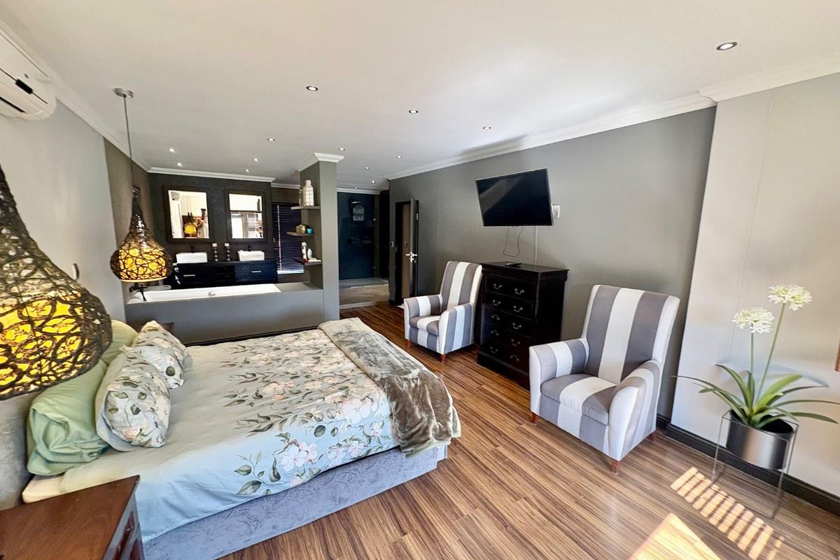 Spacious master bedroom featuring an open-plan en-suite bathroom with a built-in bathtub, double vanity, laminate flooring, and modern recessed lighting.