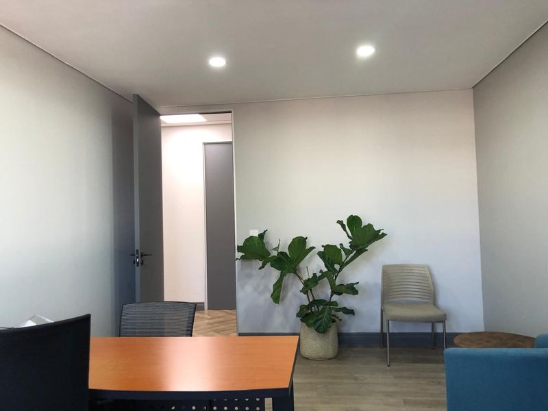 A modern office space featuring neutral walls, recessed downlighting, and durable laminate flooring with an open doorway leading to an adjacent area.