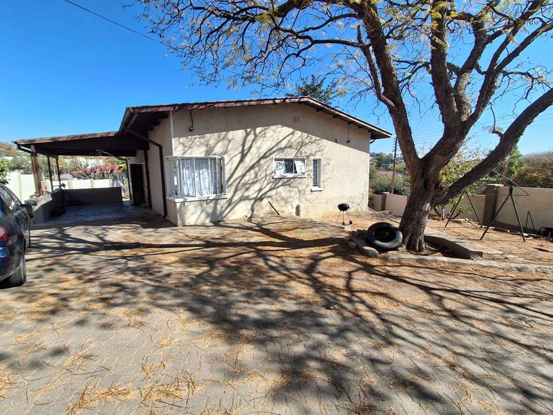 Front exterior view of a single-story house featuring a paved driveway, covered carport, and security bars on windows.
