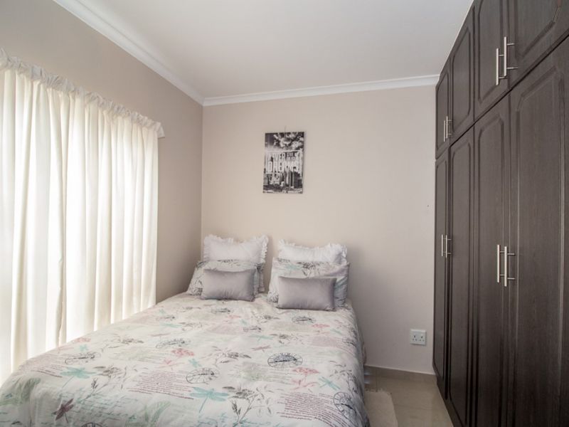 A well-maintained bedroom featuring dark wood built-in cupboards, neutral wall finishes, and tiled flooring.