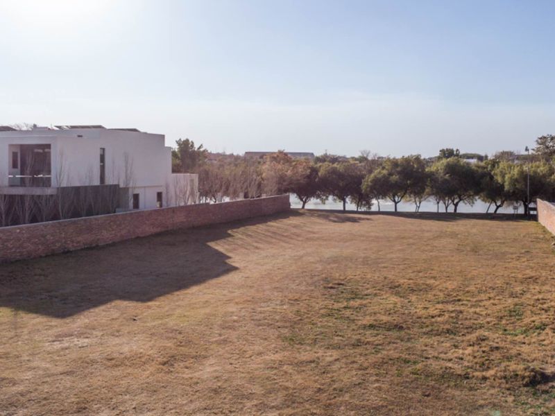 A spacious, level residential vacant land plot enclosed by brick boundary walls, offering a clear building site with established trees in the background.