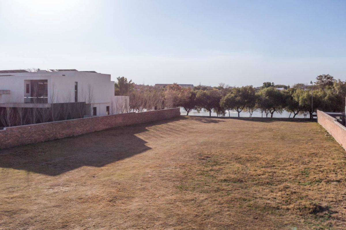 A spacious, level residential vacant land plot enclosed by brick boundary walls, offering a clear building site with established trees in the background.