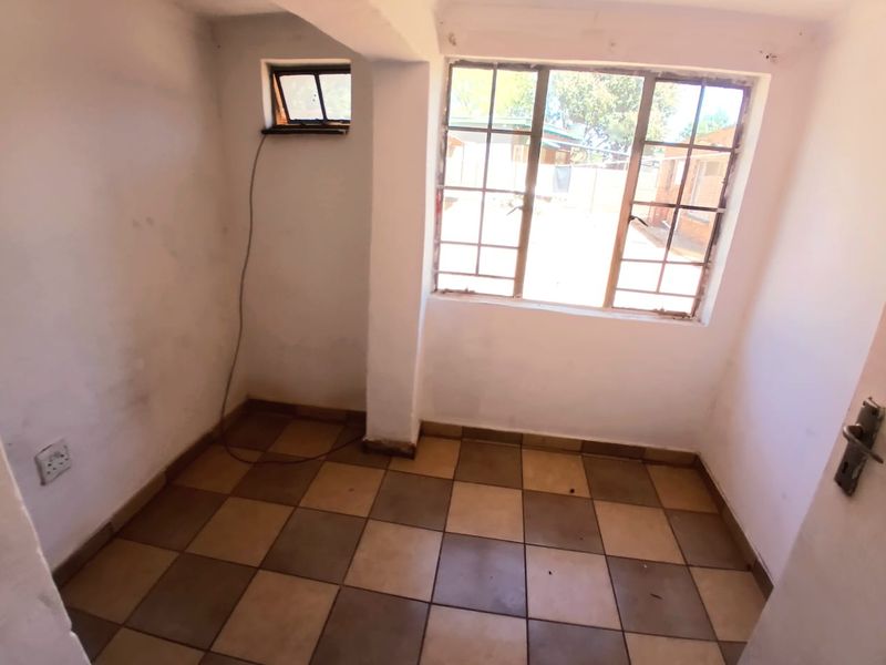 A compact, empty bedroom featuring checkered floor tiles and steel-framed windows, requiring cosmetic updates to improve its overall appeal and condition.