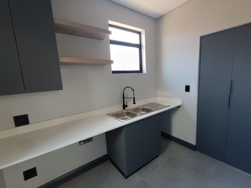 Modern scullery featuring sleek dark cabinetry, stone countertops, a double basin sink with a gooseneck tap, and floating timber shelves.