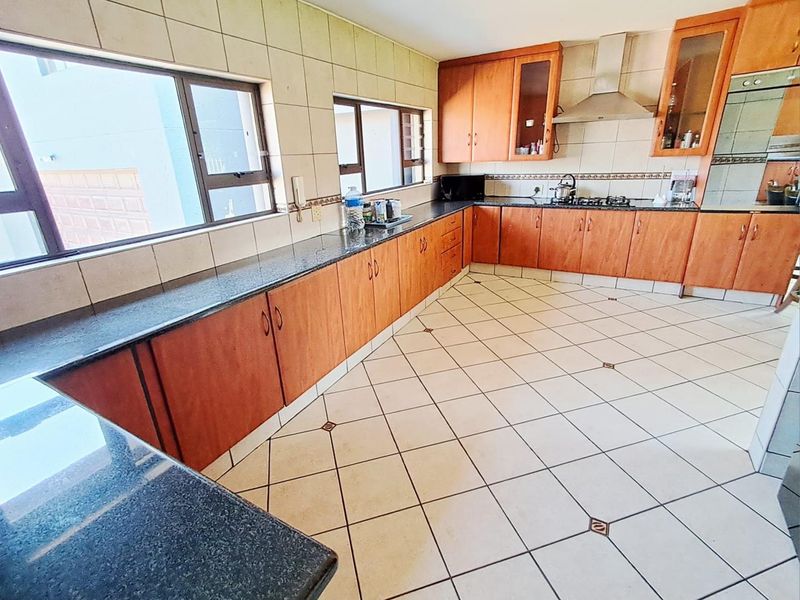Spacious kitchen featuring wooden cabinetry, granite countertops, a gas hob with extractor fan, and tiled flooring throughout.