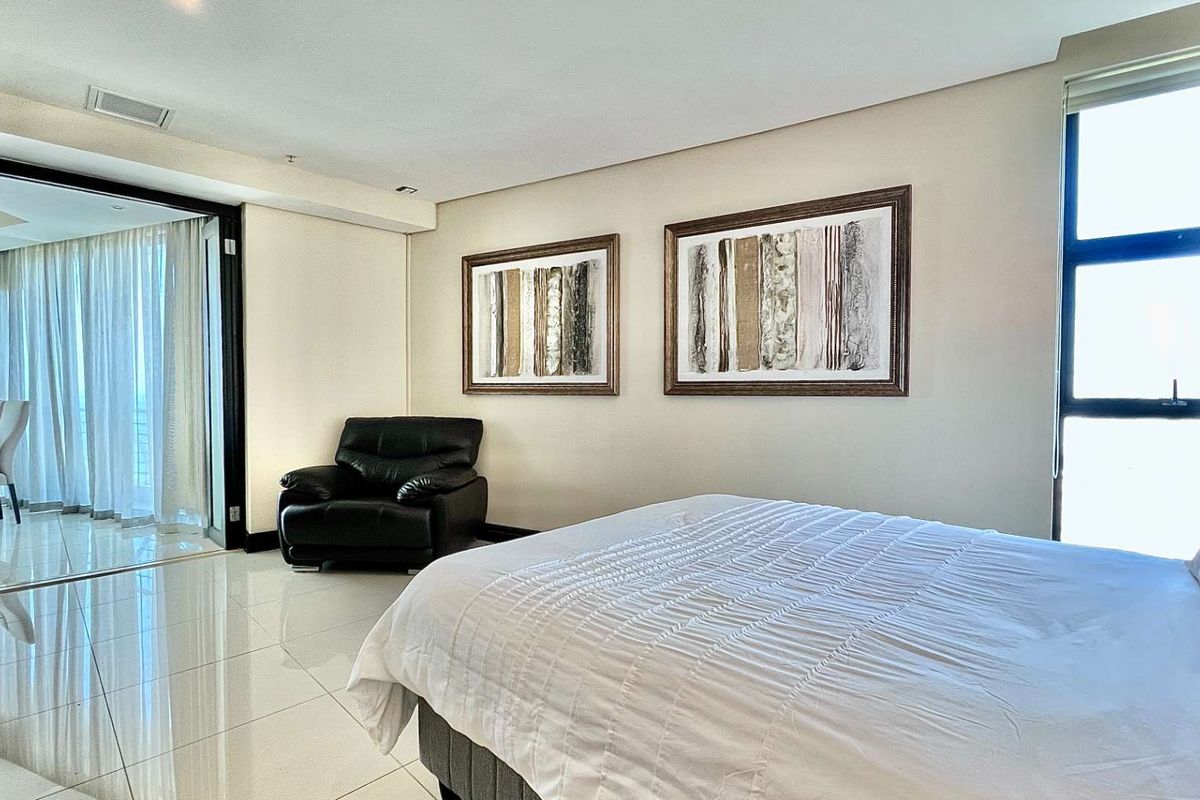 Spacious bedroom featuring polished tiled flooring, large windows for natural light, and direct access to an adjoining balcony through sliding glass doors.
