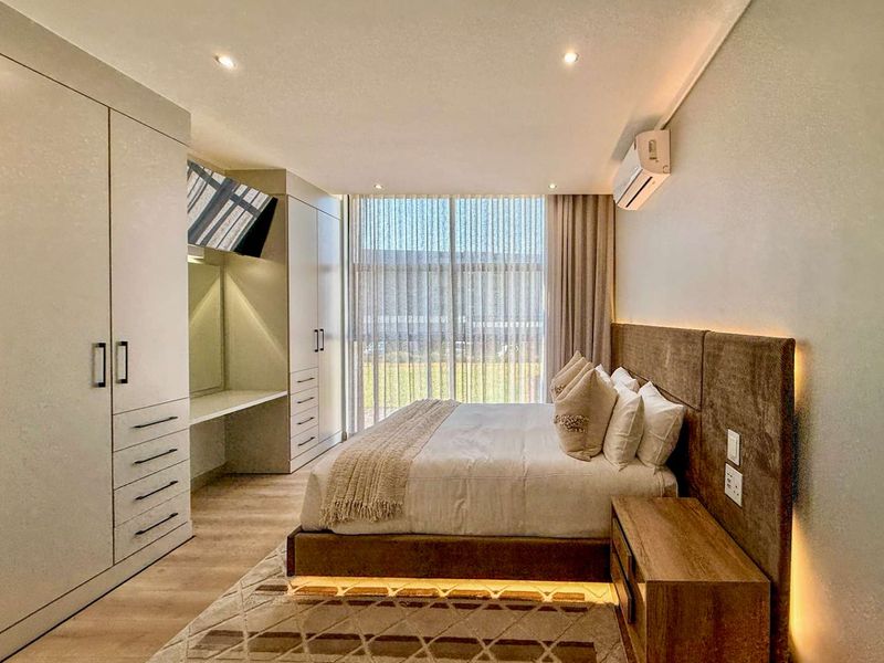 Modern bedroom featuring extensive built-in cabinetry, a custom upholstered headboard with integrated lighting, and a split-system air conditioner.