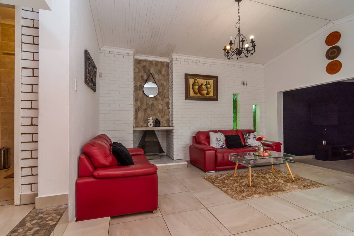 Spacious living room featuring a built-in stone fireplace, white painted brick walls, tiled flooring, and a decorative chandelier.