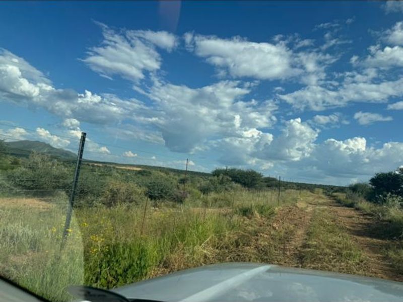 A view of the vacant residential land featuring natural vegetation, a dirt track, and wire fencing under a clear blue sky.