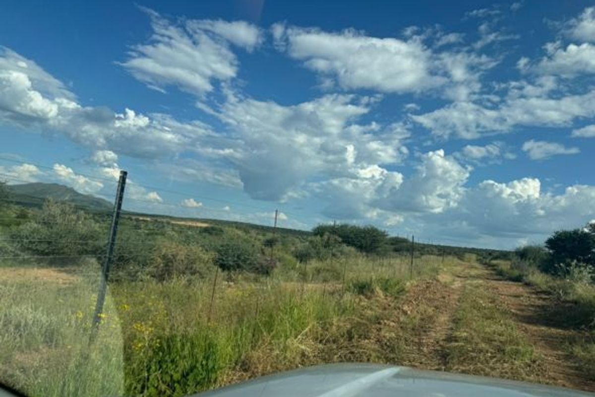 A view of the vacant residential land featuring natural vegetation, a dirt track, and wire fencing under a clear blue sky.