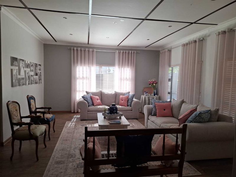 A well-maintained living room featuring laminate flooring, recessed downlighting, and large windows with venetian blinds and curtains.