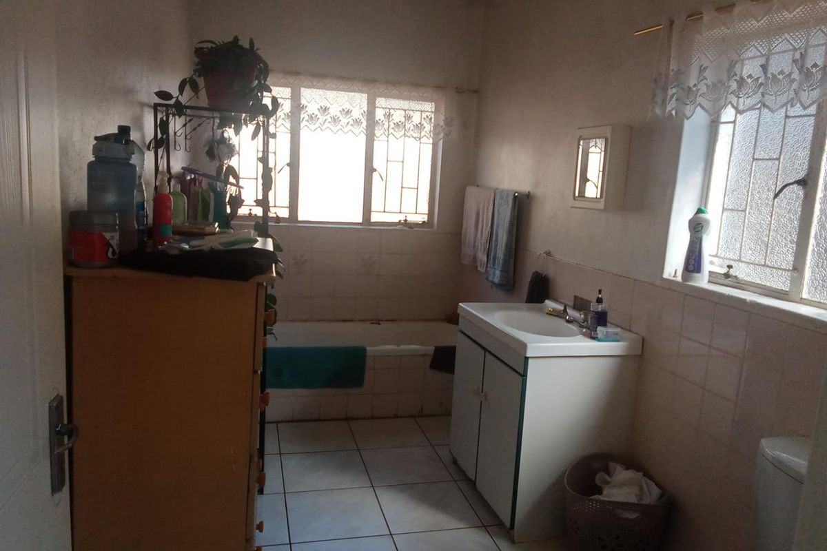 A functional bathroom featuring a built-in bathtub, vanity cabinet with integrated sink, and tiled flooring, requiring cosmetic updates to modernize the space.