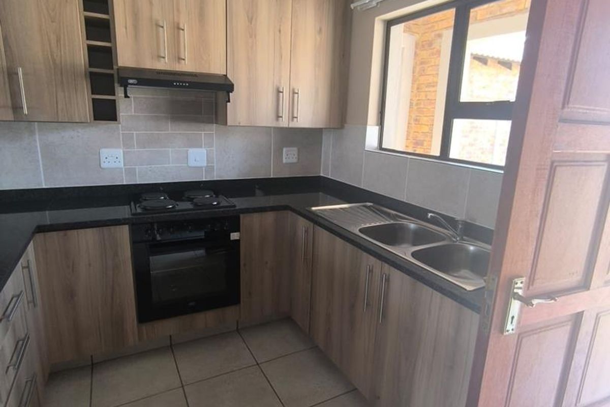 A functional kitchen featuring wood-look cabinetry, granite countertops, a built-in oven with hob, and a double bowl sink with tiled splashback.