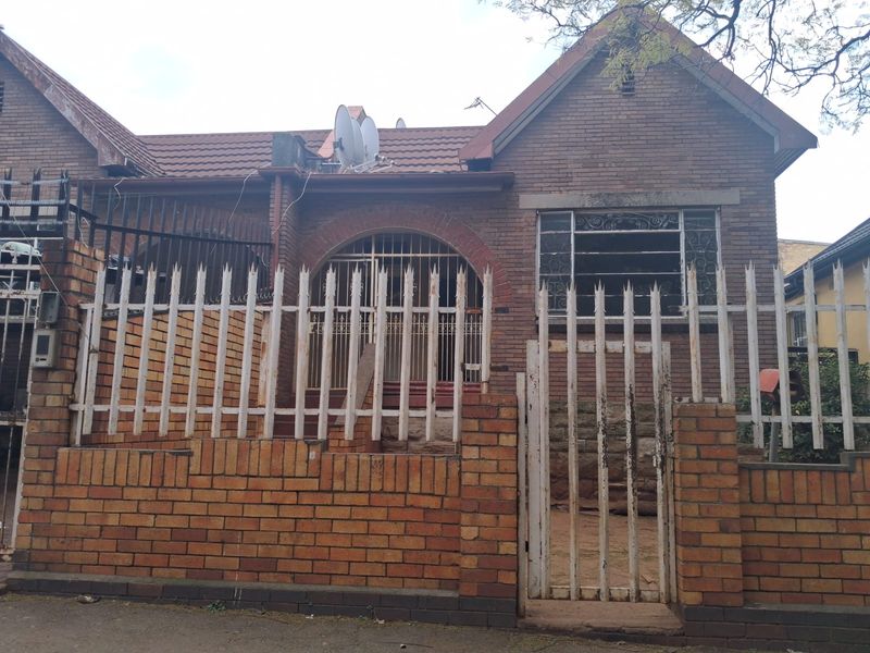 Front elevation of a brick house featuring a tiled roof, secure perimeter fencing, and a gated entrance.