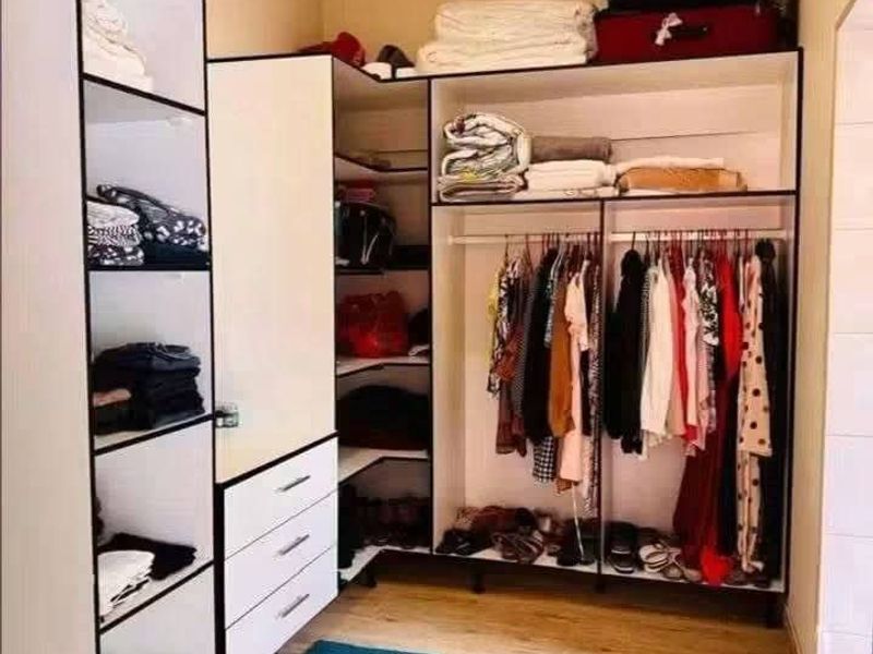 A bedroom featuring a modern, open-concept built-in wardrobe system with integrated shelving, drawers, and hanging rails, complemented by light-toned laminate flooring.