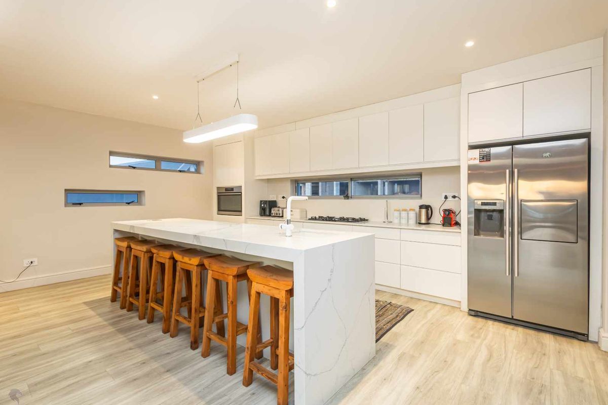 Modern kitchen featuring a large stone-topped island, sleek white cabinetry, integrated appliances, and light wood-look flooring.