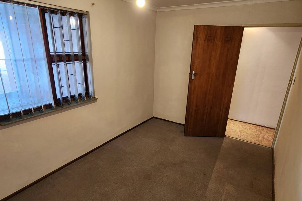 A vacant bedroom featuring neutral wall paint, carpeted flooring, and a window with security bars, providing a blank canvas for potential updates.