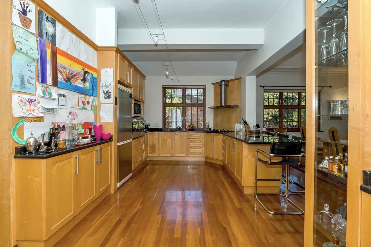 A spacious kitchen featuring light wood cabinetry, dark granite countertops, a built-in extractor fan, and polished hardwood flooring.