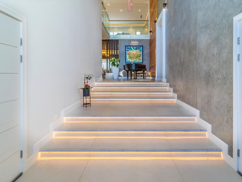 Grand entrance featuring a wide tiled staircase with integrated LED lighting, glass balustrades, and a striking concrete feature wall.