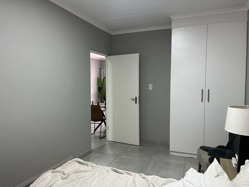 A bedroom featuring neutral grey walls, tiled flooring, and a built-in white wardrobe with modern finishes.