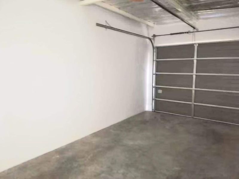 A clean, empty garage space featuring a sectional garage door, concrete flooring, and exposed ceiling structure.