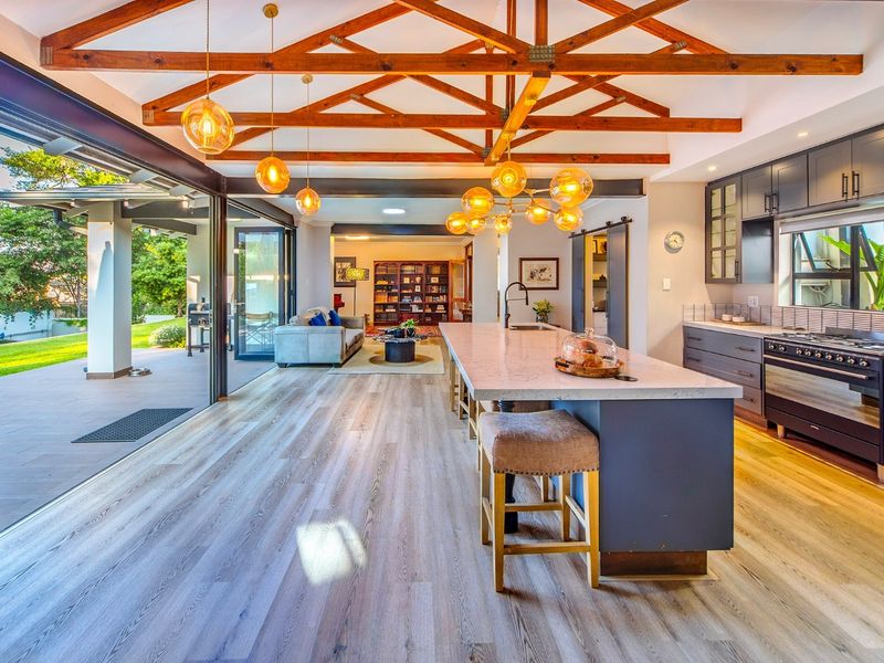 Spacious open-plan kitchen and living area featuring exposed timber trusses, a large central island, modern cabinetry, and seamless flow to the outdoor patio.