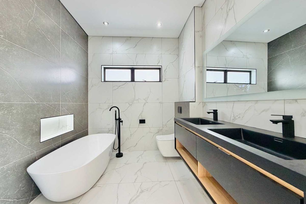 Modern luxury bathroom featuring a freestanding bathtub, double vanity with black matte fixtures, and elegant marble-look porcelain tiling throughout.