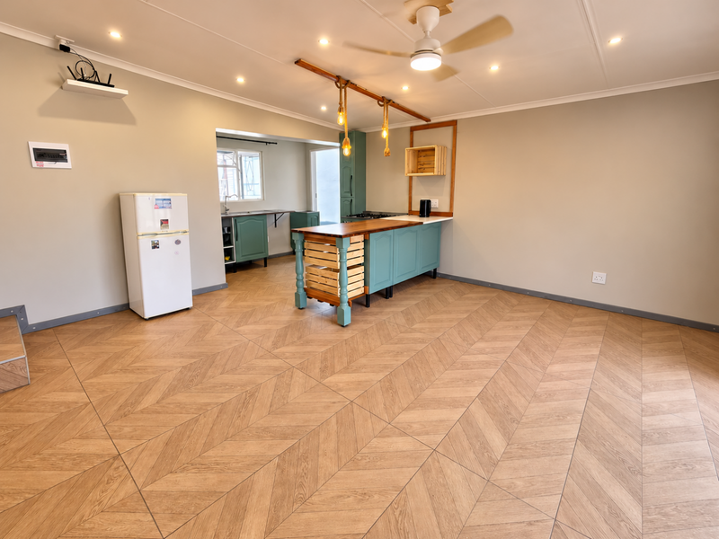 Spacious open-plan living and kitchen area featuring modern herringbone flooring, recessed lighting, and a central kitchen island with built-in cabinetry.