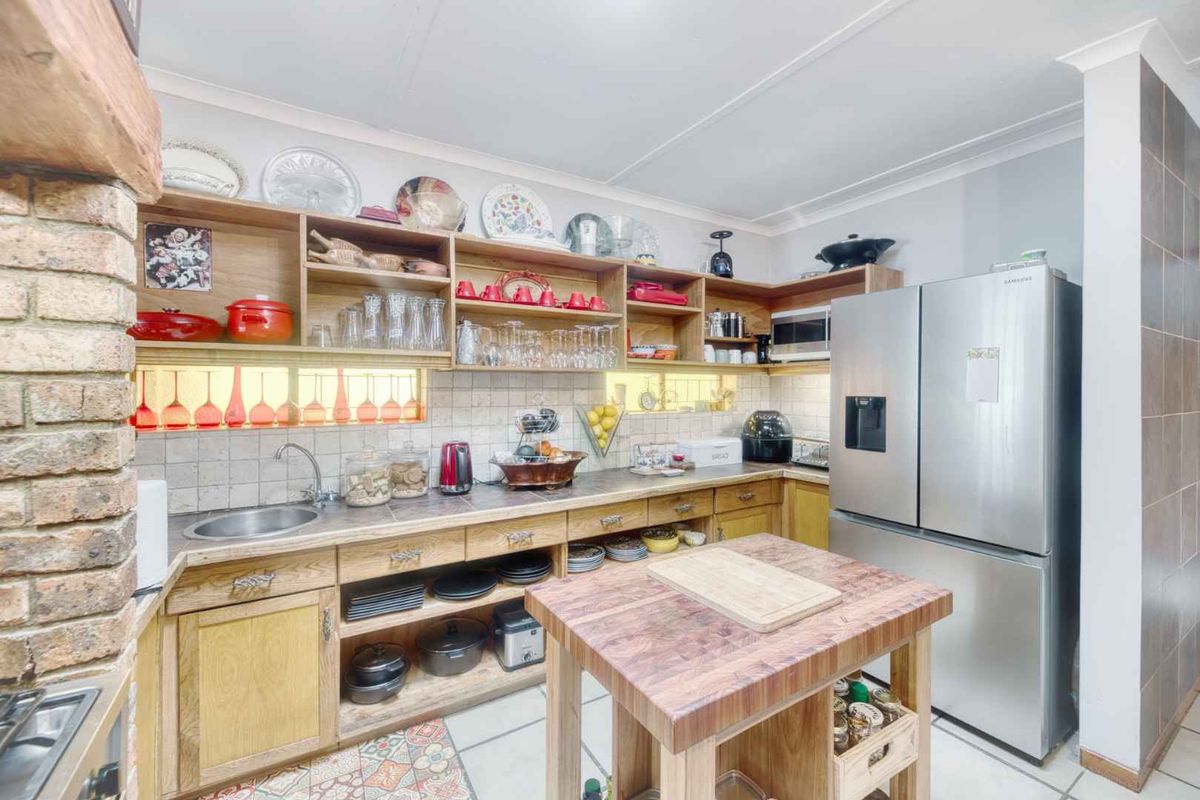 A functional kitchen featuring wooden cabinetry, open shelving, tiled backsplash, and a central wooden island, complemented by an exposed brick feature pillar.