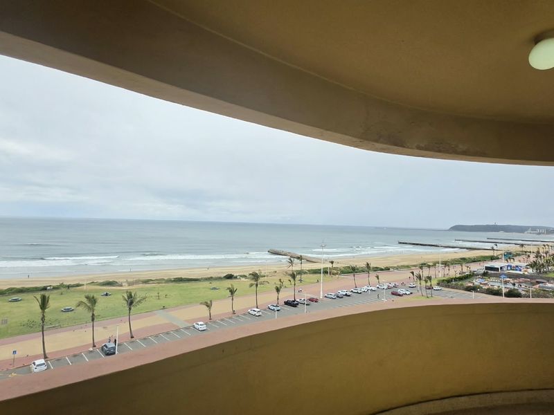 A curved balcony offering expansive views of the coastline, beach, and promenade area.