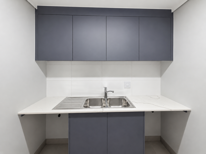 A modern, clean laundry area featuring dark grey cabinetry, a stone countertop, and a stainless steel double sink with a mixer tap.